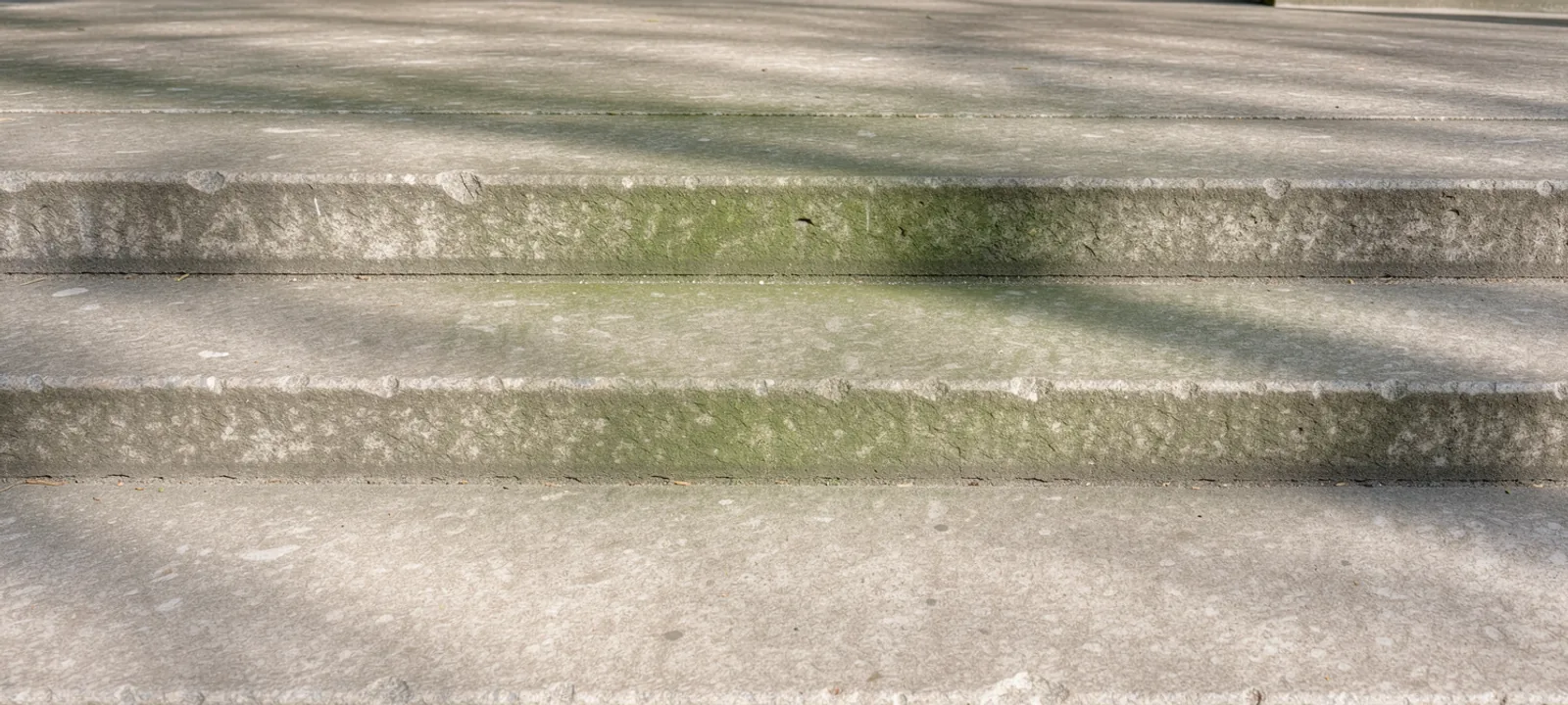 A broad outdoor stone stair crossed by soft green reflected light and a long mineral shadow